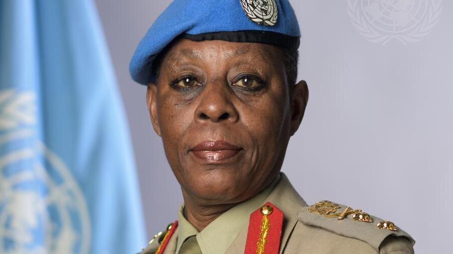 A  woman in military uniform wears a blue beret in front of the UN flag