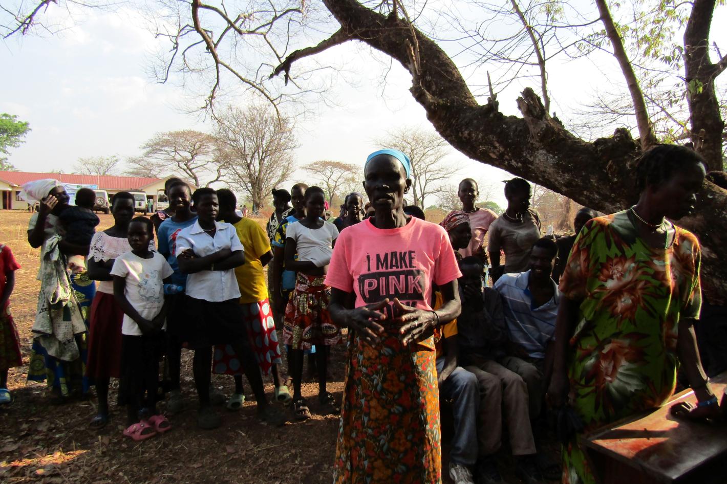 A group of women standing underneath a tree. The woman in the centre is wearing a pink t-shirt that says "I make pink"